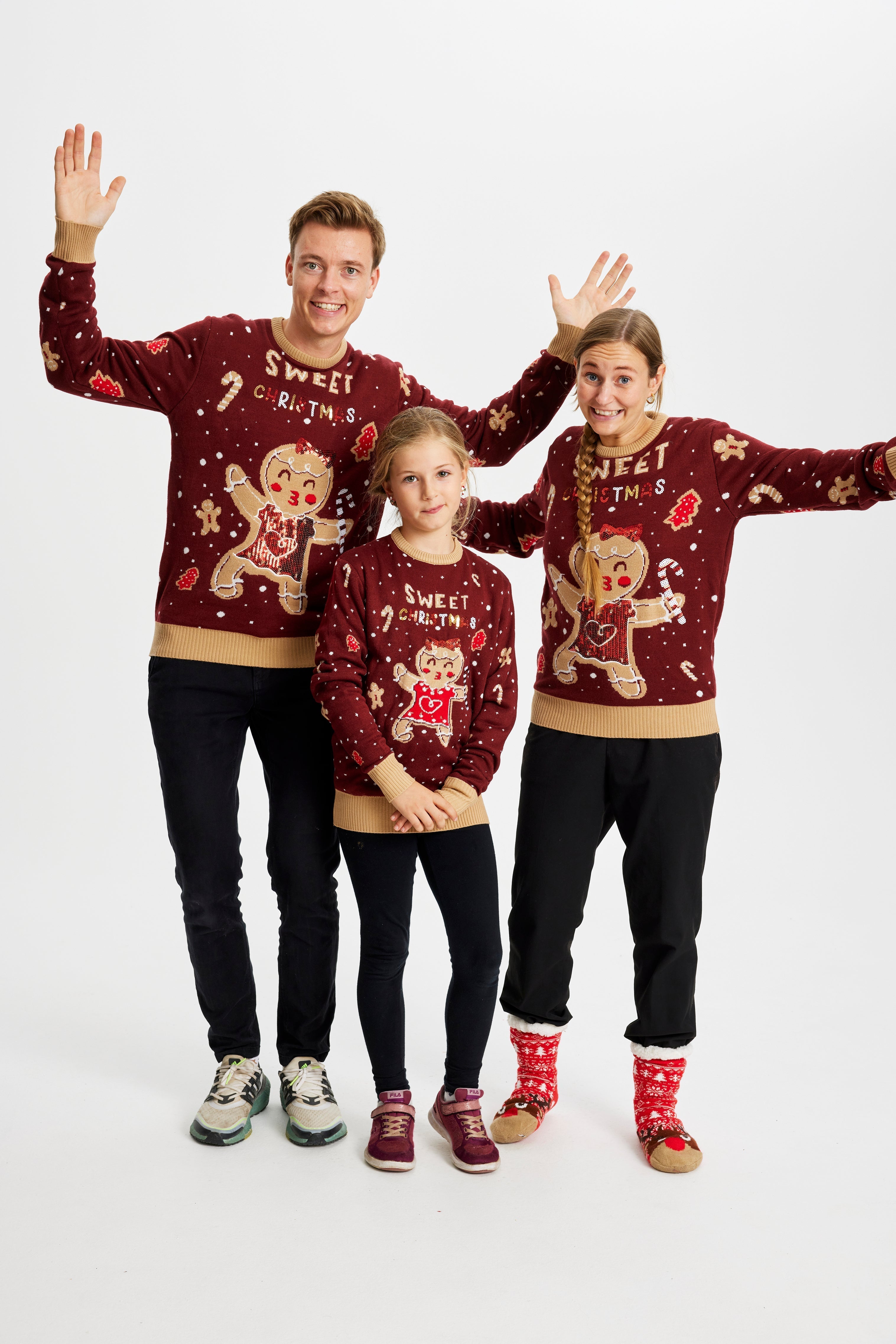 En mand, en dame og et barn poserer sammen, hver iført en mørkerød julesweater med kagepersoner og julemønster på.